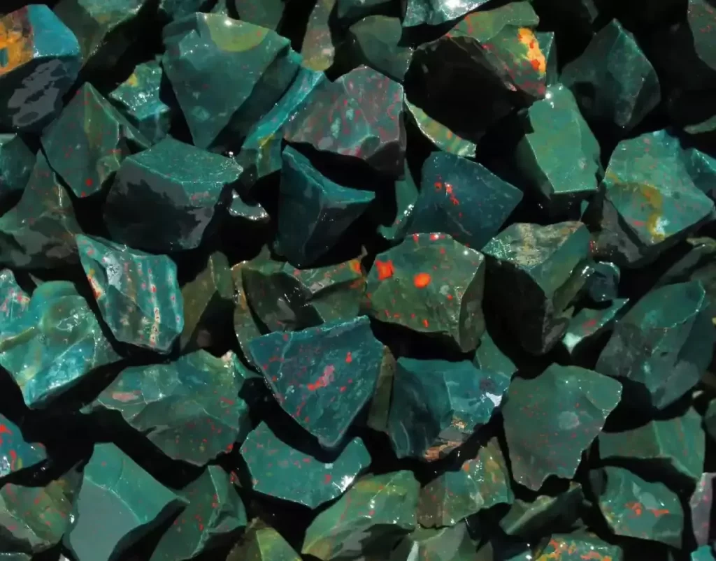 Close-up of natural bloodstone (heliotrope) tumbled stones, displaying the characteristic deep green chalcedony base with scattered red iron oxide inclusions.