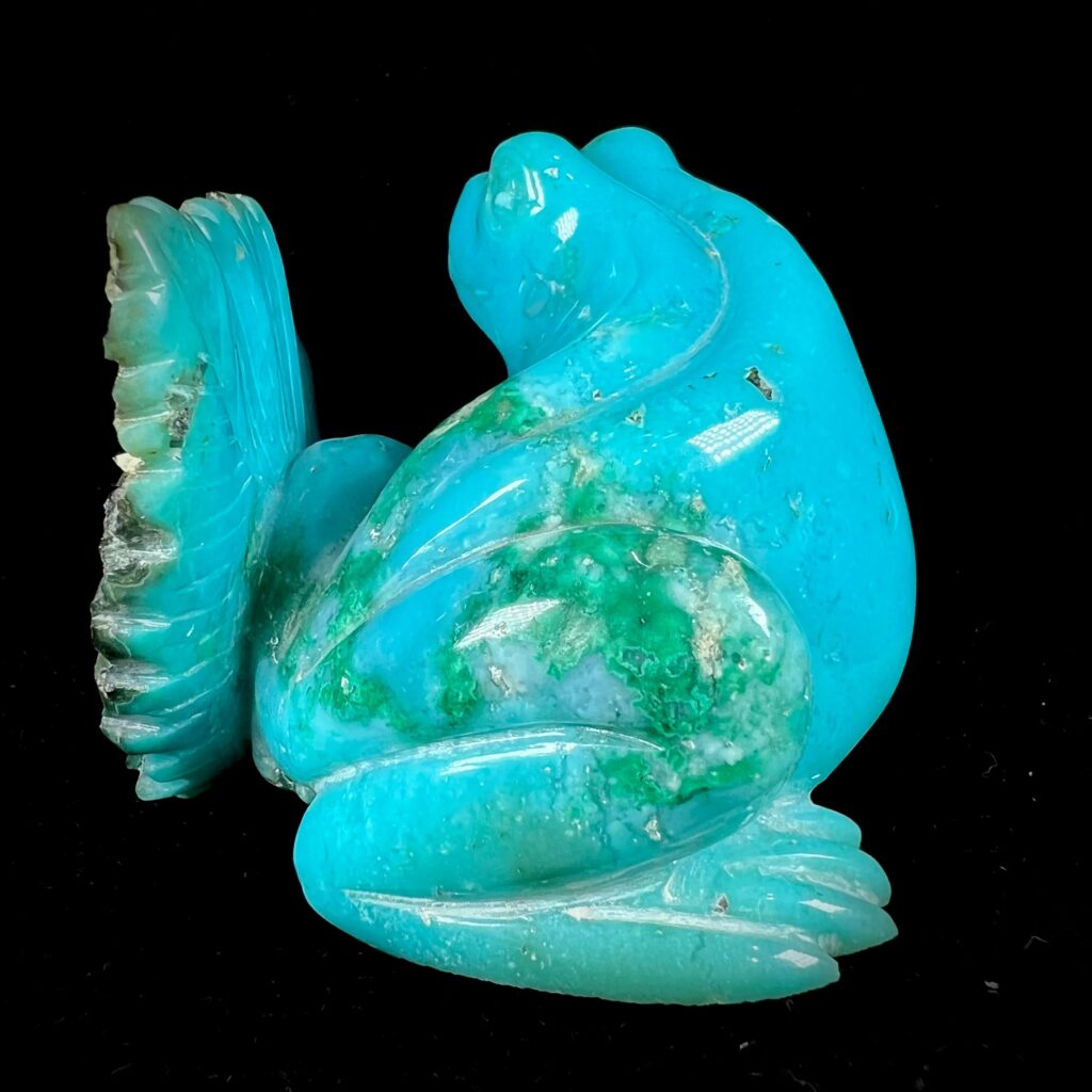 A handcrafted chrysocolla carving of a frog, displaying a smooth, polished surface with brilliant sky-blue and emerald-green marbling, set against a plain black background.