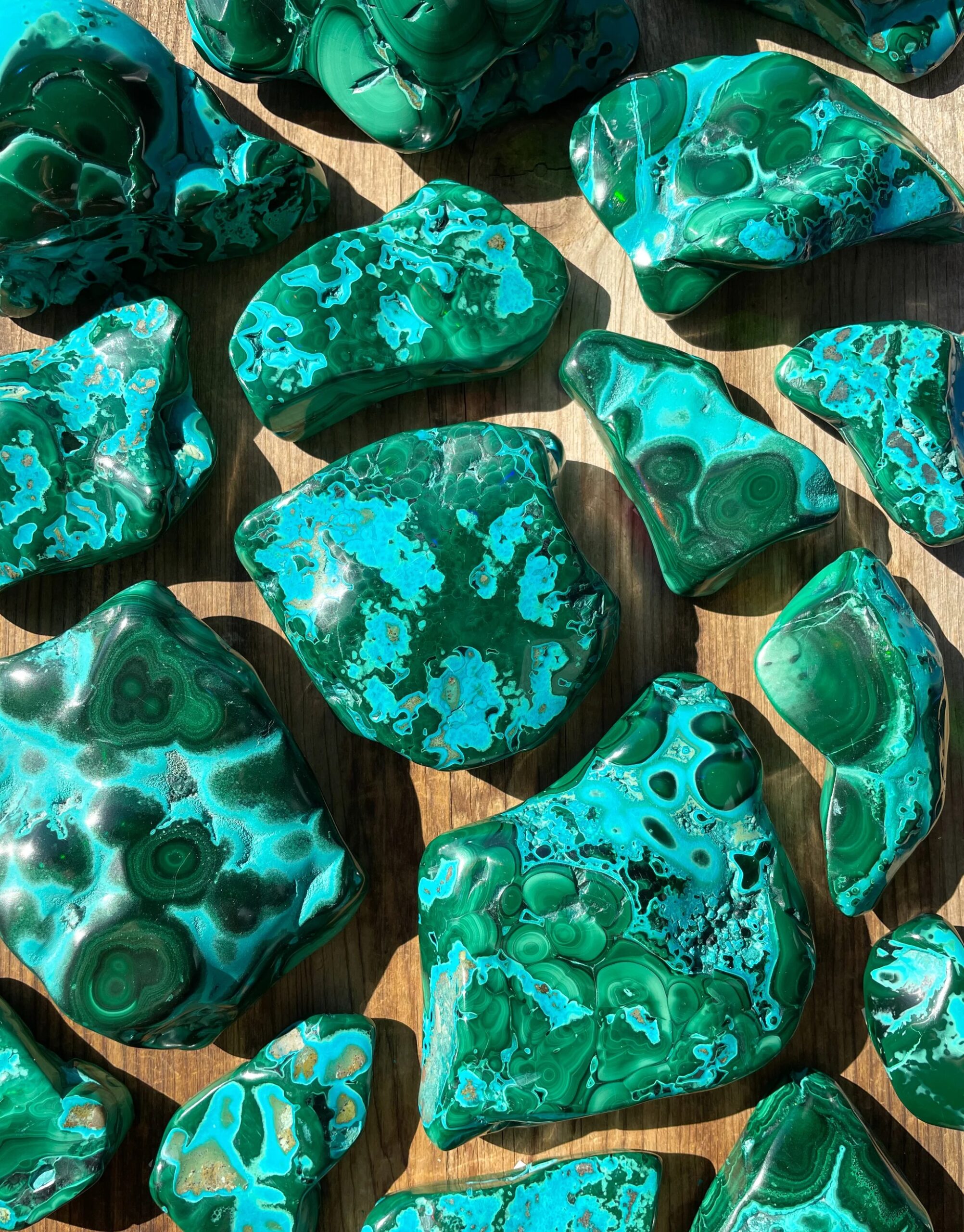 Gemini said
A collection of polished malachite and chrysocolla specimens featuring vibrant patterns of deep forest green banding and bright electric blue inclusions on a rustic wooden background.
